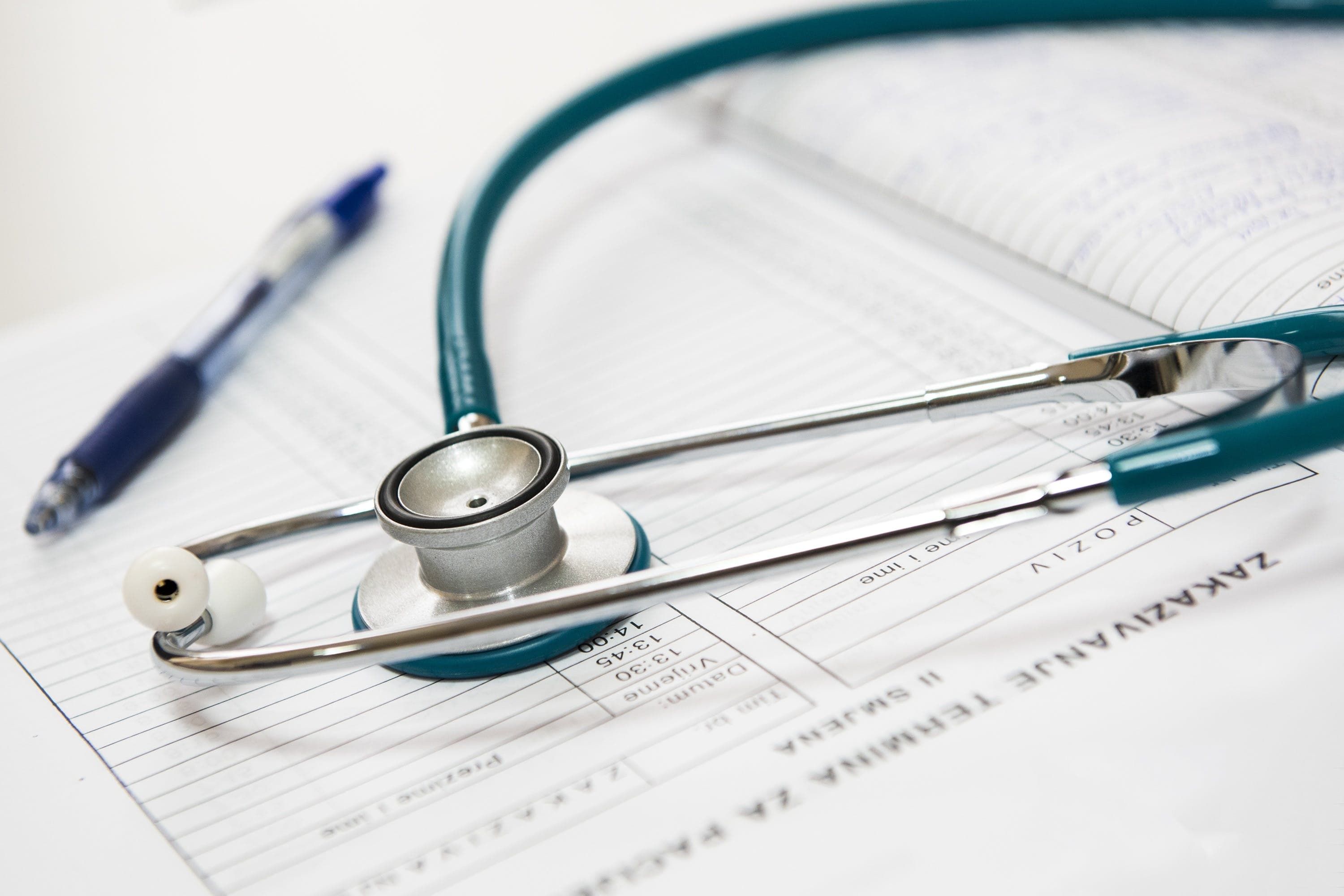 Teal stethoscope lying on a medical appointment log next to a blue ballpoint pen.